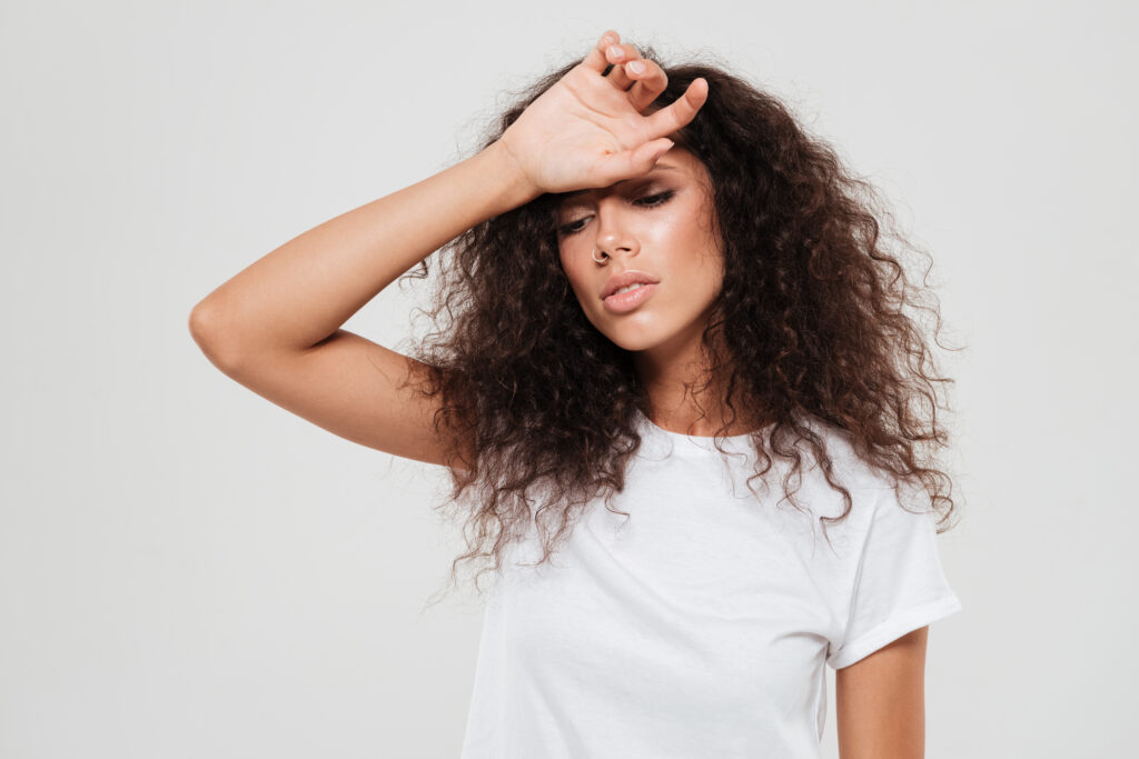 tired curly woman with closed eyes holding hand forehead