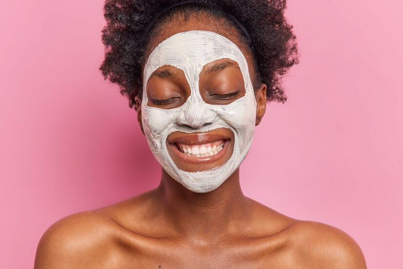 headshot positive woman smiles broadly wears white facial mask reduce pores fine lines undergoes beauty procedures poses topless against pink wall shows white teeth 273609 53539